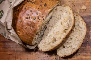 Close-up of sliced brown seeded bread on a rustic wooden cutting board with a paper bag.