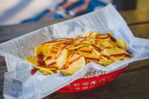 Close-up of crispy potato chips drizzled with ketchup in a red basket lined with newspaper.